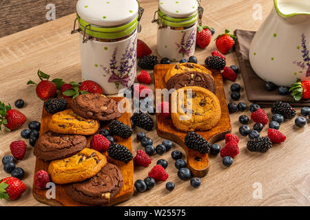 I biscotti al cioccolato su tavola di legno assortita con mix di frutti di bosco con recipienti di ceramica Foto Stock