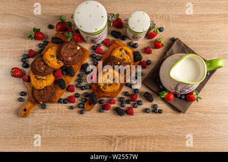 Latte in caraffa in ceramica con biscotti e bacche selvatiche sul tavolo di legno Foto Stock