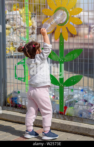 Bambina mettendo i rifiuti nel contenitore di riciclaggio. Divertente per bambini in Plastica Riciclaggio di bottiglie d'acqua. Vista posteriore. Foto Stock