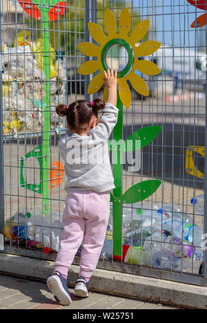 Bambina mettendo i rifiuti nel contenitore di riciclaggio. Divertente per bambini in Plastica Riciclaggio di bottiglie d'acqua. Vista posteriore. Foto Stock