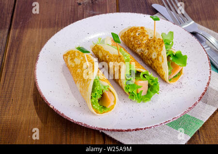 Snack rotoli da pancake, salmone e insalata verde foglie. Foto Stock