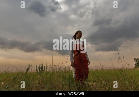 KHORTYTSIA, Ucraina - Luglio 03, 2018: Medio bianco invecchiato donna in abiti medievali passeggiate nella steppa con tuoni cielo estate sul paesaggio Khortytsia isl Foto Stock