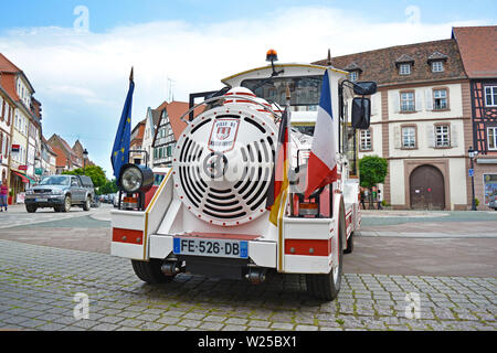 Tour di confine con il bianco touristic mini treno auto sagomata con il tedesco e il francese bandiera davanti, in piedi sulla piazza del mercato a Wissembourg Francia Foto Stock