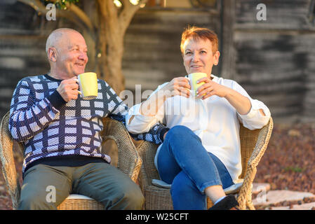 Sorridente anziano uomo e donna su sedie in giardino esterno, vacanza. Coppia senior relax presso il parco sulla giornata di sole.Amare vecchia coppia bere il caffè. Foto Stock