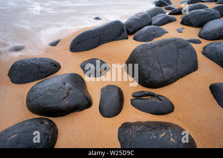 Massi di dolerite su Embleton Bay beach con il Mare del Nord in lavaggio, Northumberland, Inghilterra Foto Stock
