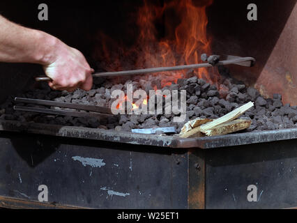 Fabbro al lavoro la formazione di metallo caldo dopo il riscaldamento in una fucina. Foto Stock