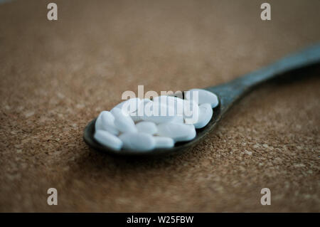 Bianco pillole di prodotti farmaceutici e medicinali in il cucchiaio di legno su un sughero marrone dello sfondo. Valentines, cuore, malati, salute e il concetto di guarigione. Foto Stock