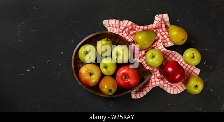 Vista del piano portapaziente, scolpito in legno ciotola con le mele e le pere, tovaglie, sul marmo nero come bordo, spazio per il testo sul lato sinistro Foto Stock