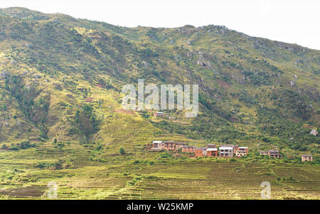 Tipico paesaggio del Madagascar nella regione vicino Ambohimanjaka. Terreno con piccole colline rocciose ricoperte di cespugli e pochi alberi, rosso case di argilla, riso Foto Stock