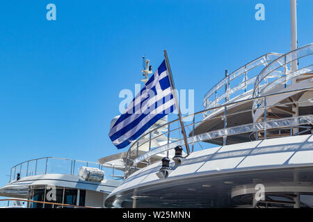 Bandiera Greca su yacht di lusso stern. Crociera in corso in Grecia. Cielo azzurro sfondo, vista ravvicinata. Foto Stock