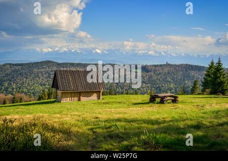 Molla bellissimo paesaggio rurale. Capanna in legno in una radura con un lead per snow-capped alte montagne. Foto Stock