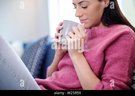 Giovane donna rilassante sul divano con bevanda calda Foto Stock