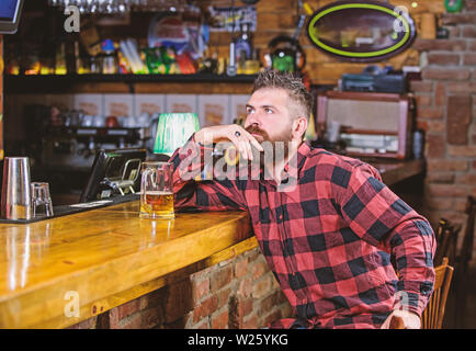 Ordine di bere alcol. Il bar è un luogo rilassante hanno bere e rilassarsi. Uomo con barba trascorrere il tempo libero nella barra di colore scuro. Brutale parigamba uomo barbuto sedersi al banco bar bere birra. Hipster rilassante presso il bar con birra. Foto Stock