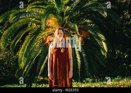 Attraente giovane donna in piedi meditando nella parte anteriore di un tropical Palm tree in La Concepción Historical-Botanical Giardini in Malaga Foto Stock