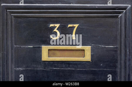 Casa numero 37 con le trentasette in cifre di metallo su una tavola di legno porta anteriore con il letterbox in bronzo Foto Stock