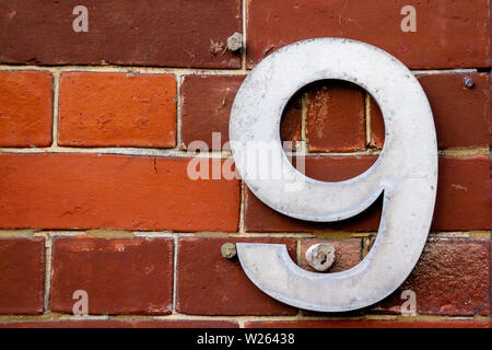 Numero civico 9 con le nove in metallo su cifre in rosso di un muro di mattoni Foto Stock