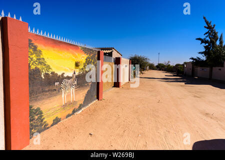 Casa con una grande parete, cancelli, un murale di una zebra e picchi di corrente in una cittadina alla periferia di Otjiwarongo, Namibia Foto Stock