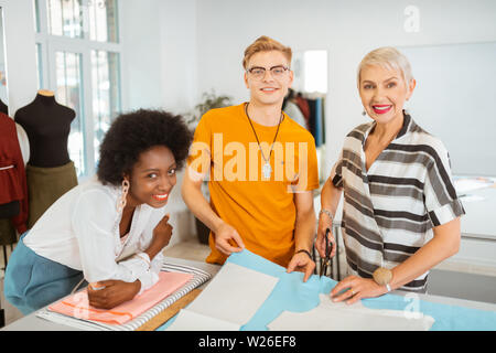 Le persone felici. Lieta professional tailors sorridere mentre in piedi accanto al tavolo di taglio in un fashion designer studio Foto Stock