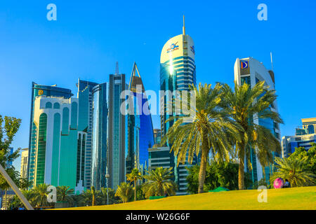 Doha, Qatar - 20 Febbraio 2019: palme in West Bay Sheraton Park lungo la corniche, con vetrate si erge alta. Medio Oriente, Penisola arabica Foto Stock