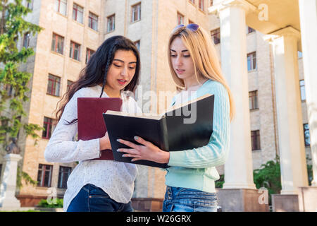 Due belle gli studenti di diverse nazionalità stanno studiando un libro di testo presso il palazzo dell'università Foto Stock