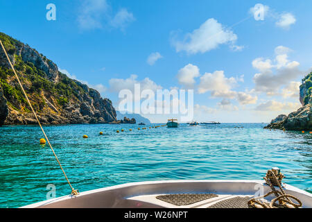 Una piccola barca che si dirige verso altre barche e al di fuori della baia di Palaiokastritsa verso il Mare Egeo sull'isola di Corfu Grecia. Foto Stock