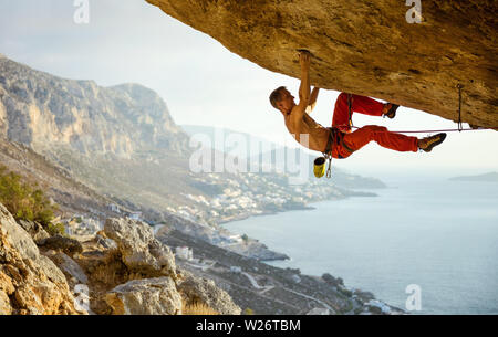 Giovani caucasici uomo arrampicata percorso impegnativo in grotta contro la bella vista della costa Foto Stock