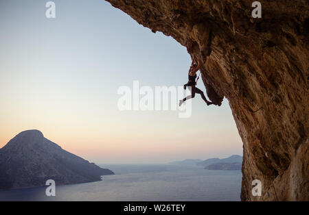 Giovani caucasici donna arrampicata percorso impegnativo al tramonto Foto Stock