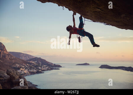 Giovane uomo che lottano per salire sulla sporgenza cliff, vista della costa sottostante Foto Stock