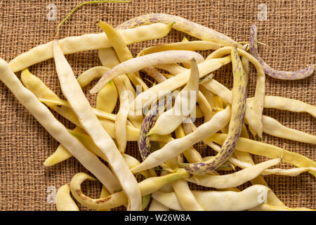 Organico giallo piatto di fagioli di cera pila sul tessuto di iuta sfondo. Foto Stock