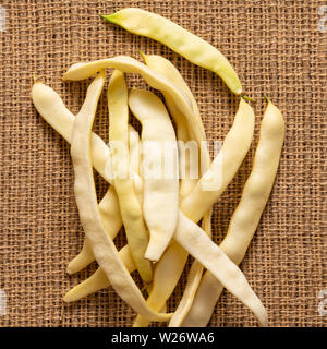 Organico giallo piatto di fagioli di cera pila sul tessuto di iuta sfondo. Foto Stock