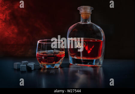 Pub ancora la vita di acquavite in un bicchiere e decanter a fianco di shungite nero blocchi di refrigerazione o riutilizzabili di cubetti di ghiaccio contro un smokey backgroun atmosferica Foto Stock