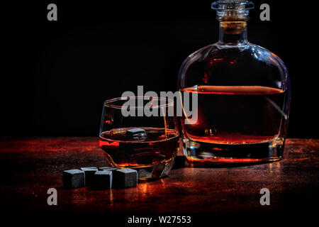 Bottiglia incandescente e decanter di whisky di malto con nero riutilizzabili i blocchi di ghiaccio o cubetti di refrigerazione su di un legno rustico bancone bar con sfondo spazio di copia Foto Stock