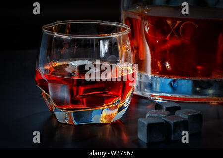 Incandescente un bicchiere di whiskey con cubetti di refrigerazione o riutilizzabili blocchi di ghiaccio e il decanter su un contatore di pub in una vista ravvicinata Foto Stock