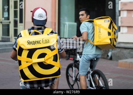 Mosca, Russia - Luglio 2, 2019, la consegna del cibo a Mosca - corriere in un cappello con earflaps e una giacca gialla con iscrizione Yandex cibo e giallo ba Foto Stock