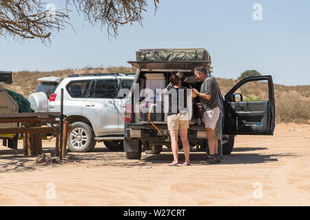 Giovane o di un uomo e di una donna di disimballare il loro 4x4 camping off road veicolo terrestre a un campeggio area picnic in Kgalagadi Parco transfrontaliero, Sud Africa Foto Stock