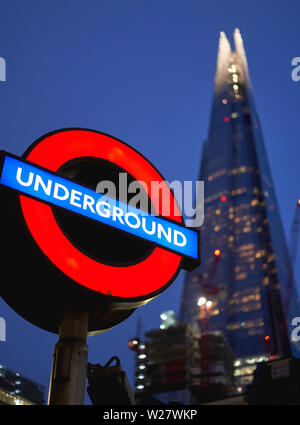 London, Regno Unito - Febbraio, 2019. Un tipico segno della metropolitana con la Shard sullo sfondo al tramonto. Foto Stock