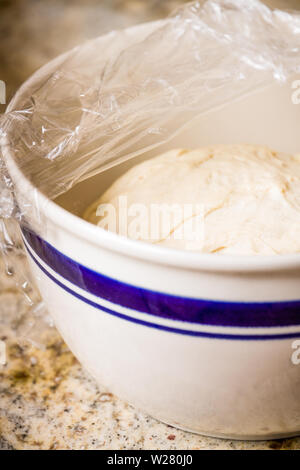 In casa pasta della pizza in aumento in una terrina ricoperta con pellicola di plastica fino a quando il volume non sarà raddoppiato Foto Stock
