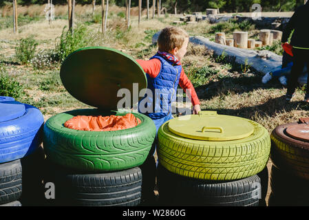 Bambini che giocano attorno a cassonetti per il riciclaggio realizzate con materiali di riutilizzo. Foto Stock