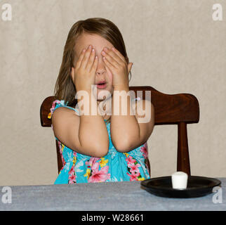 Un giovane bambino seduti ad un tavolo aspettando pazientemente per un marshmallow Foto Stock