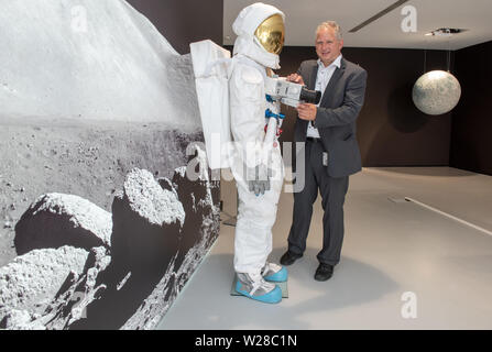 Oberkochen, Germania. 01 Luglio, 2019. Vladan Blahnik, testa lente di sviluppo, sorge accanto ad una tuta spaziale nel Museo Zeiss, il quale è montato con un Hasselblad medio formato fotocamera con un obiettivo Carl Zeiss®. La società sveva sviluppato speciali lenti per la NASA Moonlight Programma, con la quale, tra le altre cose, la prima foto sono state scattate sulla luna nel luglio 1969. (A DPA: 'lenti per la luna" - lenti dell'Apollo voli proveniva dalla Svevia') Credito: Stefan Puchner/dpa/Alamy Live News Foto Stock