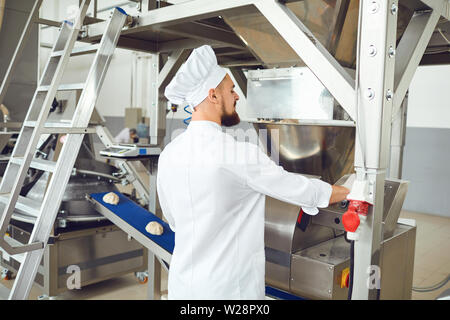 Un baker in bianco uniforme controlla il processo di creazione di impasto per la cottura del pane presso la fabbrica di panetteria. Foto Stock