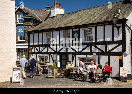 Regno Unito, Cumbria, Hawkshead, Main Street, i clienti sat nella luce del sole al di fuori di testa della regina Inn Foto Stock