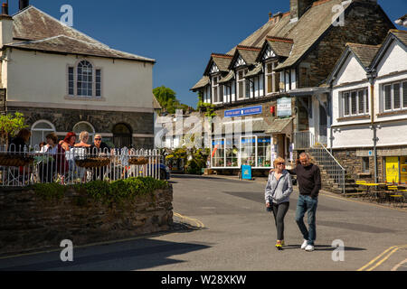 Regno Unito, Cumbria, Hawkshead, la piazza e i visitatori a piedi passato Peter Rabbit e amici shop negozio e clienti sat nella luce del sole al di fuori cafe Foto Stock