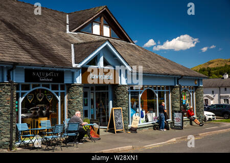 Regno Unito, Cumbria, Hawkshead, Hawkshead outdoor negozio di abbigliamento e naturalmente Hawkshead cafe con il cliente seduto al sole al tavolo esterno Foto Stock