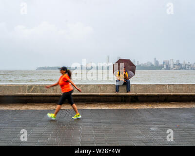 Mumbai, India - 30 Giugno 2019 : Unidentifed tourist area con posti a sedere con ombrellone e guardare le persone che la mattina a piedi / fare jogging a Marine Drive promenade Foto Stock