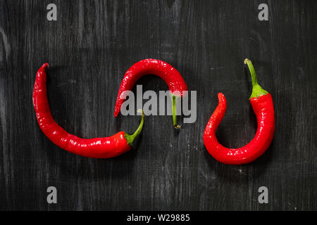 Tre chili peppers su sfondo nero, vista dall'alto. Sparse laici piatto di peperoncino al buio su un tavolo di legno Foto Stock