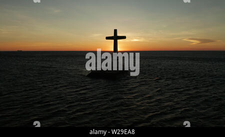 Croce cattolica nel cimitero affondata nel mare al tramonto, Vista aerea. Colorato nubi luminose durante il tramonto sul mare. Tramonto al cimitero affondata Camiguin Island Filippine. Foto Stock