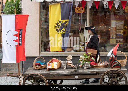 Sonneberg, Germania. 07 Luglio, 2019. Tradizionalmente un vestito uomo cammina passato un negozio decorata con bandiere di Franconia (l) e Sonneberg alla 'Day di Franconia 2019', che avviene per la prima volta in Franconia-influenzato la regione della Turingia. Con il 'Day dei Franchi' della Franconia distretti amministrativi ricordare la fondazione della Franconia circolo imperiale nell'anno 1500. Credito: Michael Reichel/dpa/Alamy Live News Foto Stock