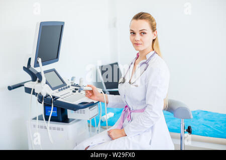 Giovane donna bionda medico con lo stetoscopio sul suo collo ubicazione vicino a macchina ad ultrasuoni Foto Stock