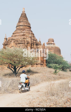 Uomo che cavalca scooter elettrico verso i templi e pagode di antica Bagan in Myanmar. Orientamento verticale Foto Stock